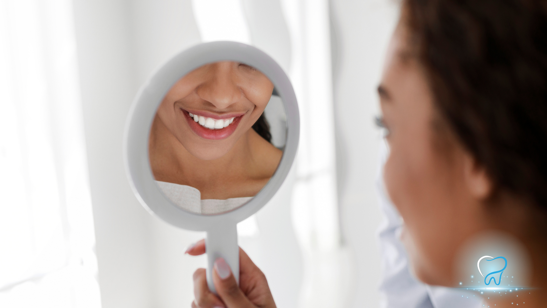 A woman is looking at her smile in a hand mirror.