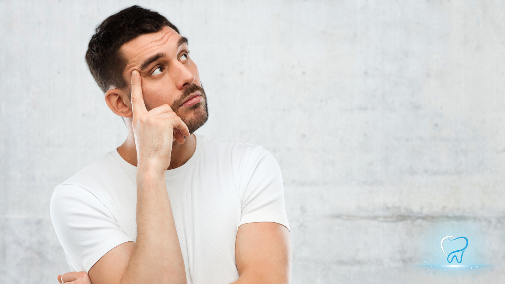 A man in a white shirt is holding his finger to his forehead and looking up.