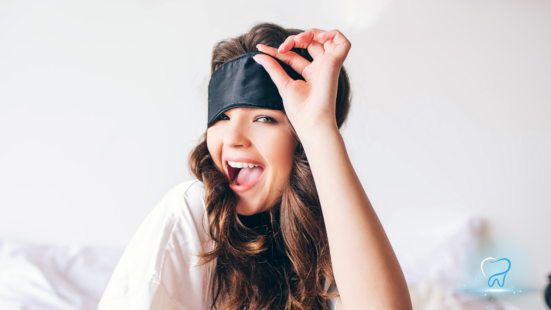 A woman wearing a sleep mask is sitting on a bed.