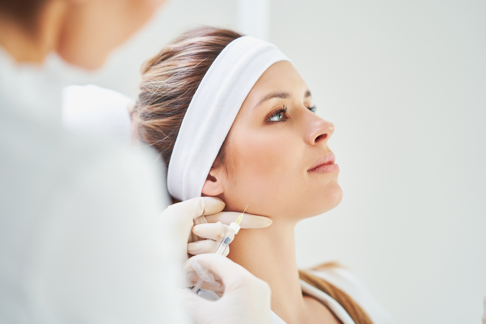 Woman receiving an injection in her neck, wearing a white headband, in a medical setting.