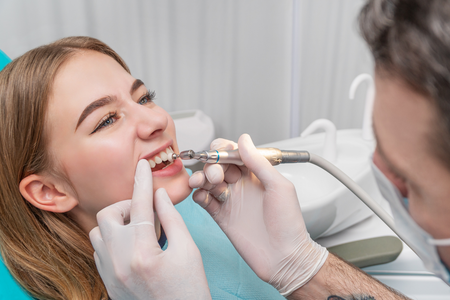 Dentist examining a smiling patient’s teeth with a dental tool in a clinic