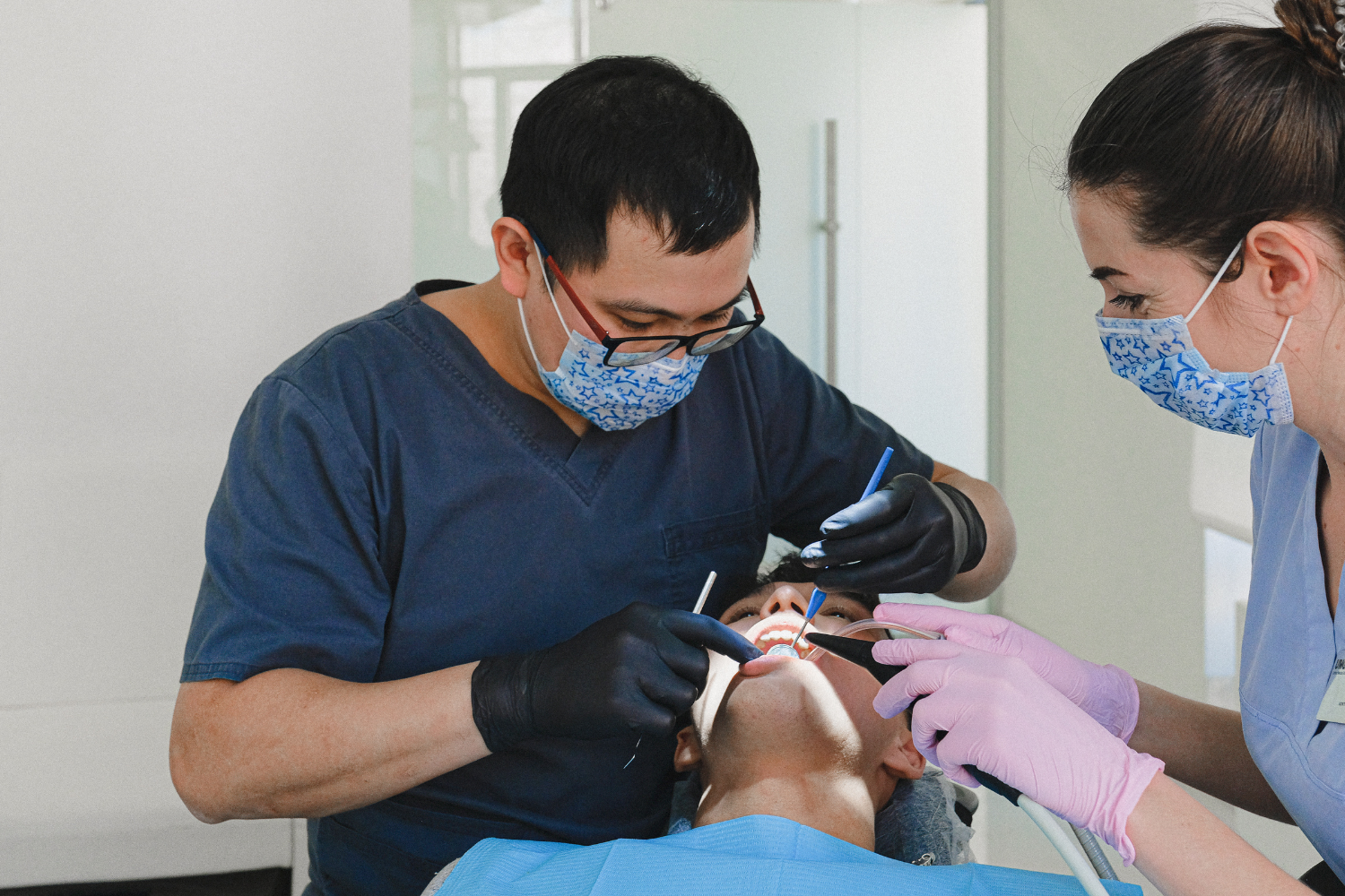 Dentists wearing masks and gloves treating a patient in a dental chair