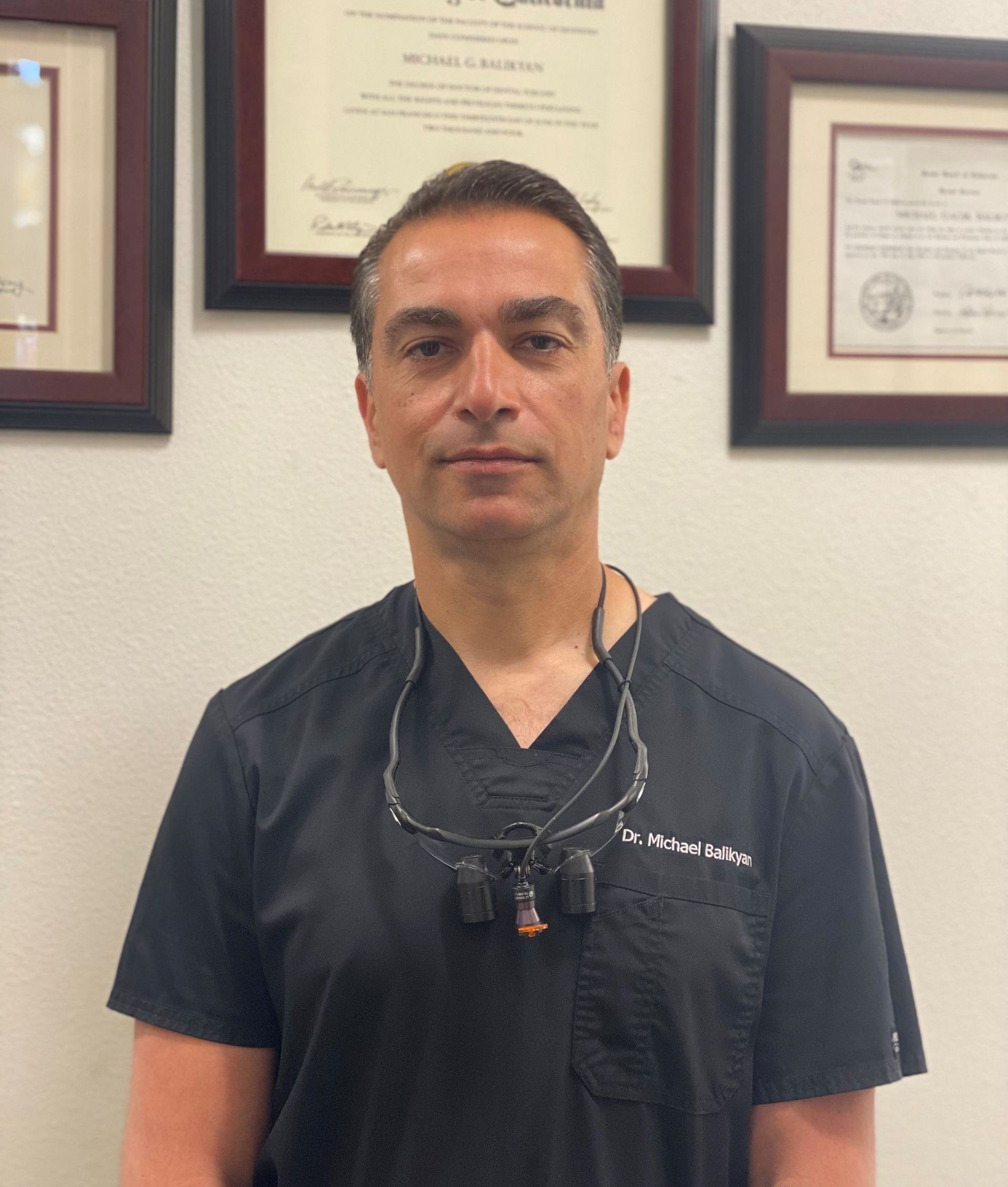 A man in a blue shirt and tie smiles in front of a computer monitor
