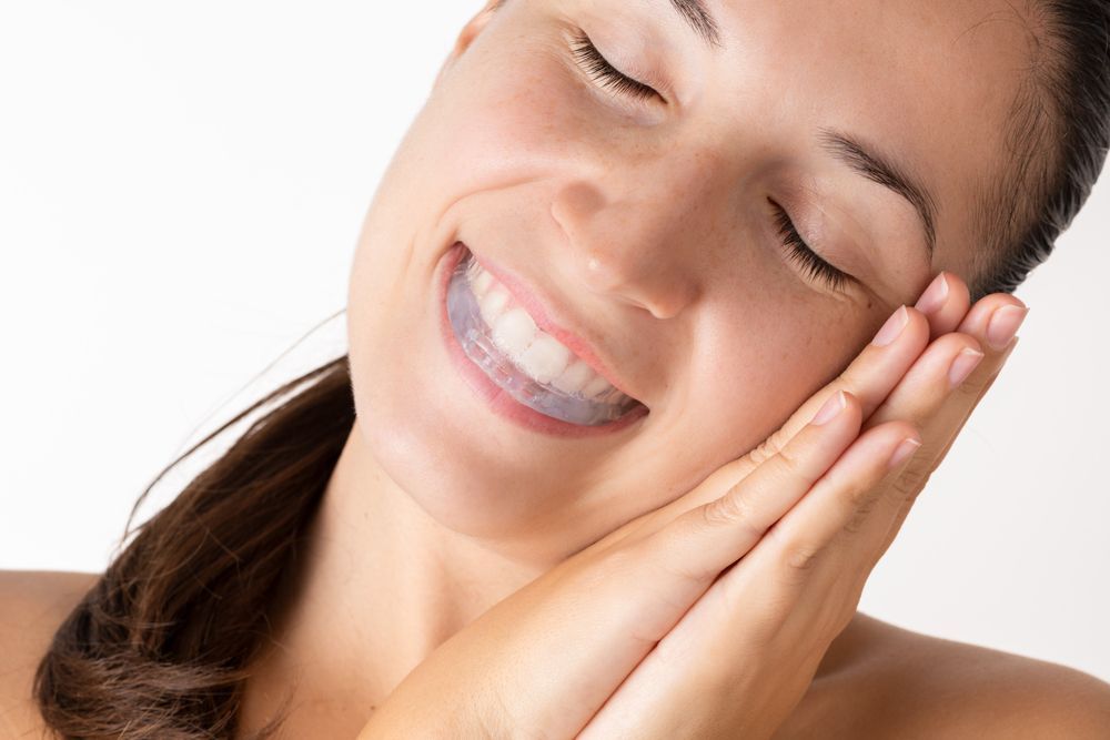 Smiling person with eyes closed, gently pressing hands to cheek on a white background