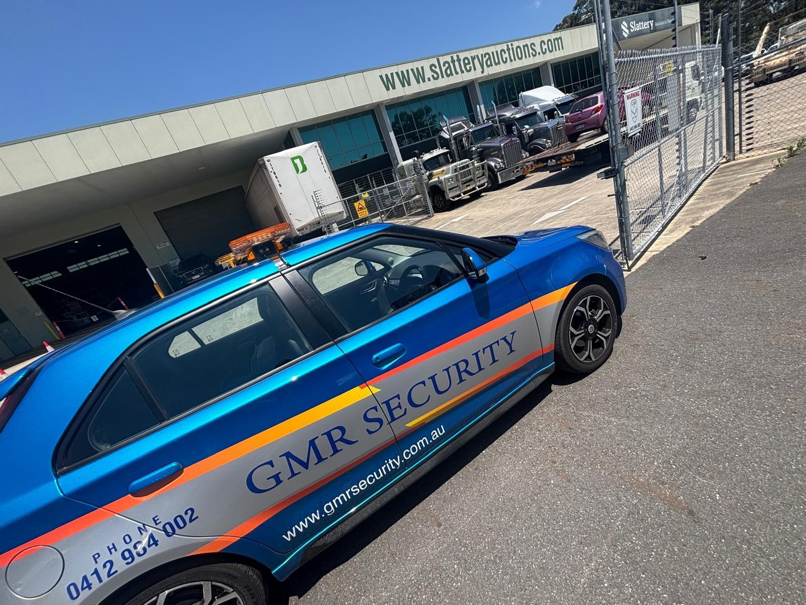Blue GMR Security car parked in front of a business. The car has orange and yellow stripes.