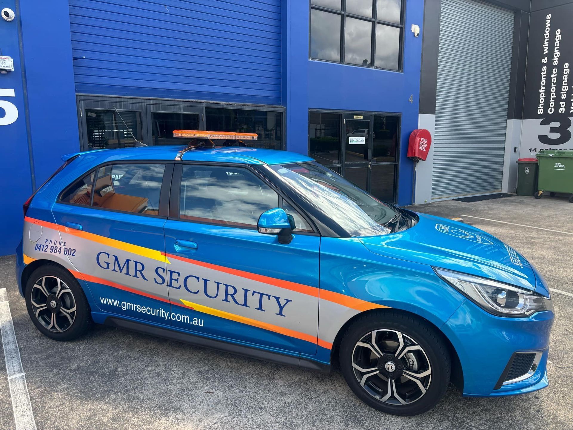 Blue GMR Security car parked in front of a warehouse.