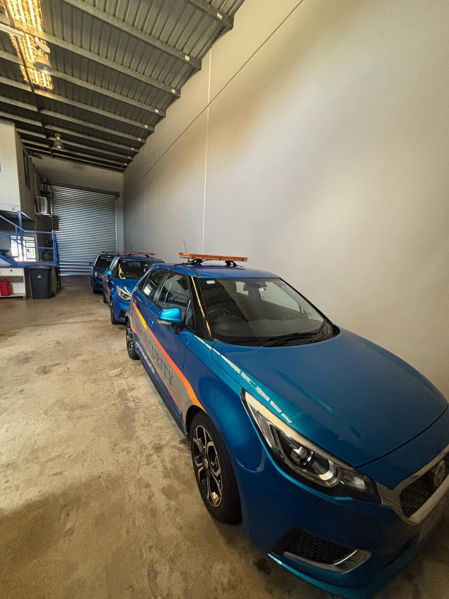 Blue cars parked in a long garage, with a roller door visible in the distance.