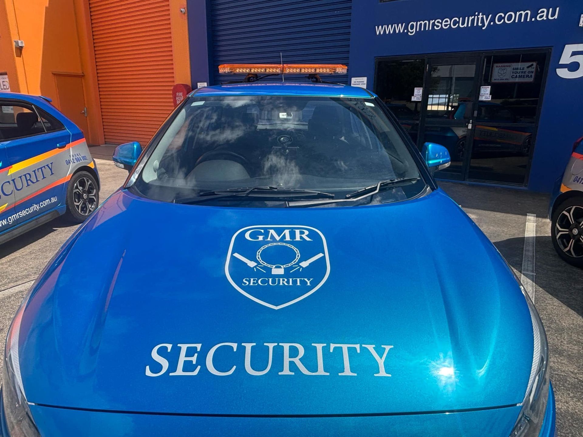 Blue security car with the GMR Security logo parked outside a building.