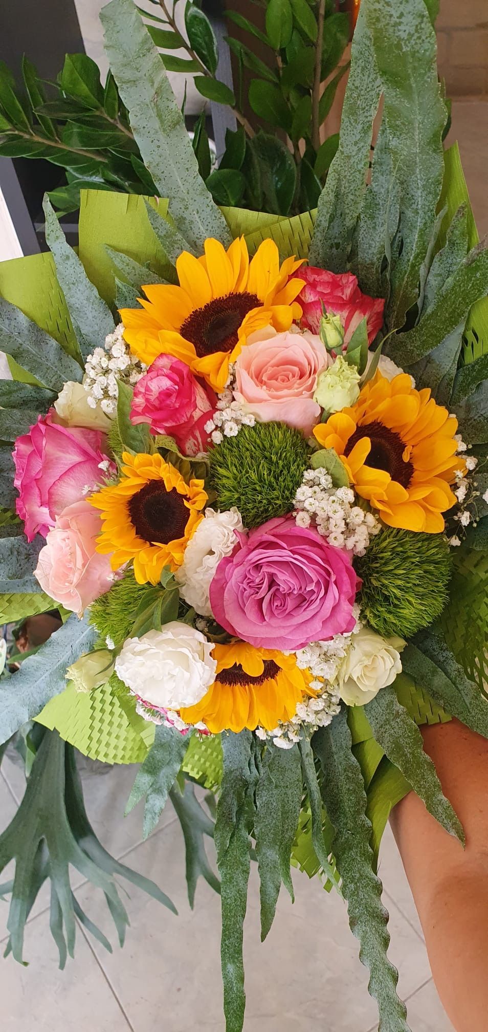 Un bouquet di fiori colorati con girasoli, rose e varie piante verdi.