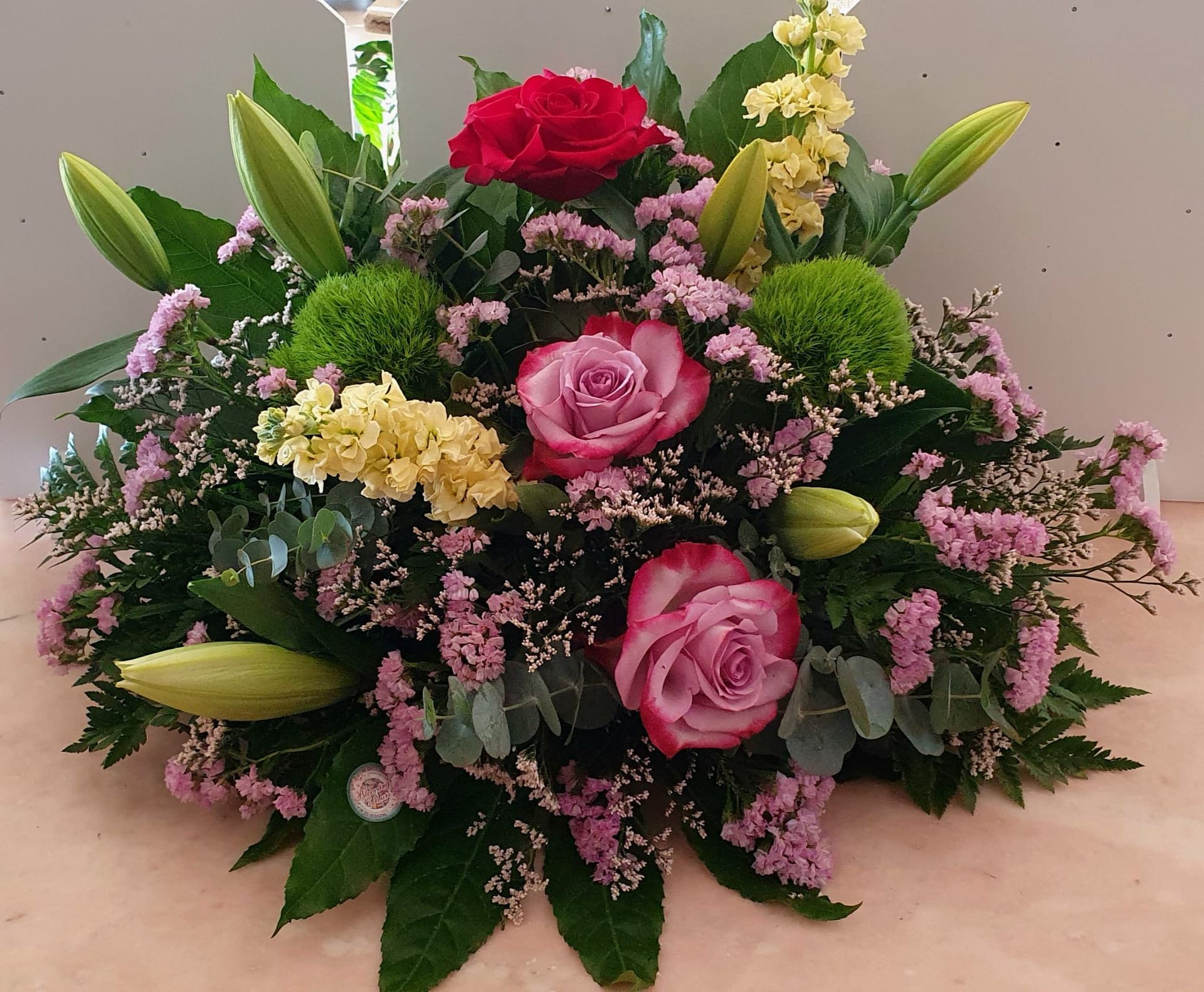 Composizione floreale con rose rosse, rosa e gialle, accenti verdi e viola.