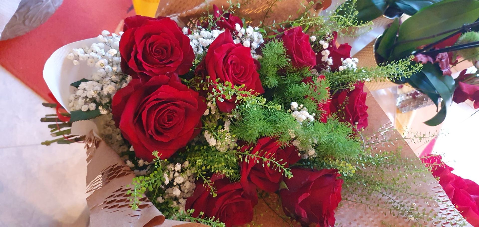 Bouquet di rose rosse con dettagli bianchi e verdi. Avvolto in carta decorativa.