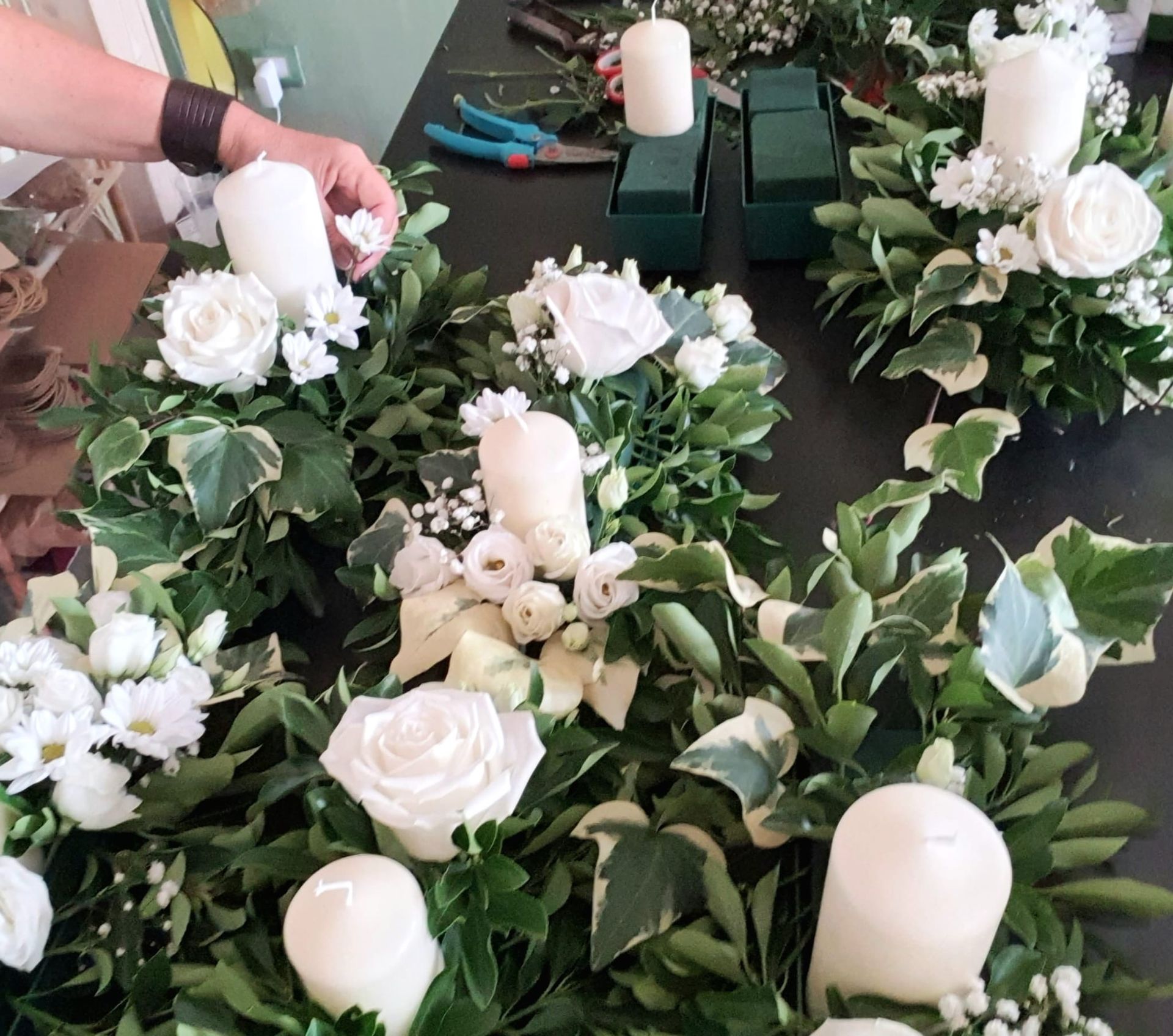 Persona che dispone fiori bianchi, candele e verde su un tavolo.
