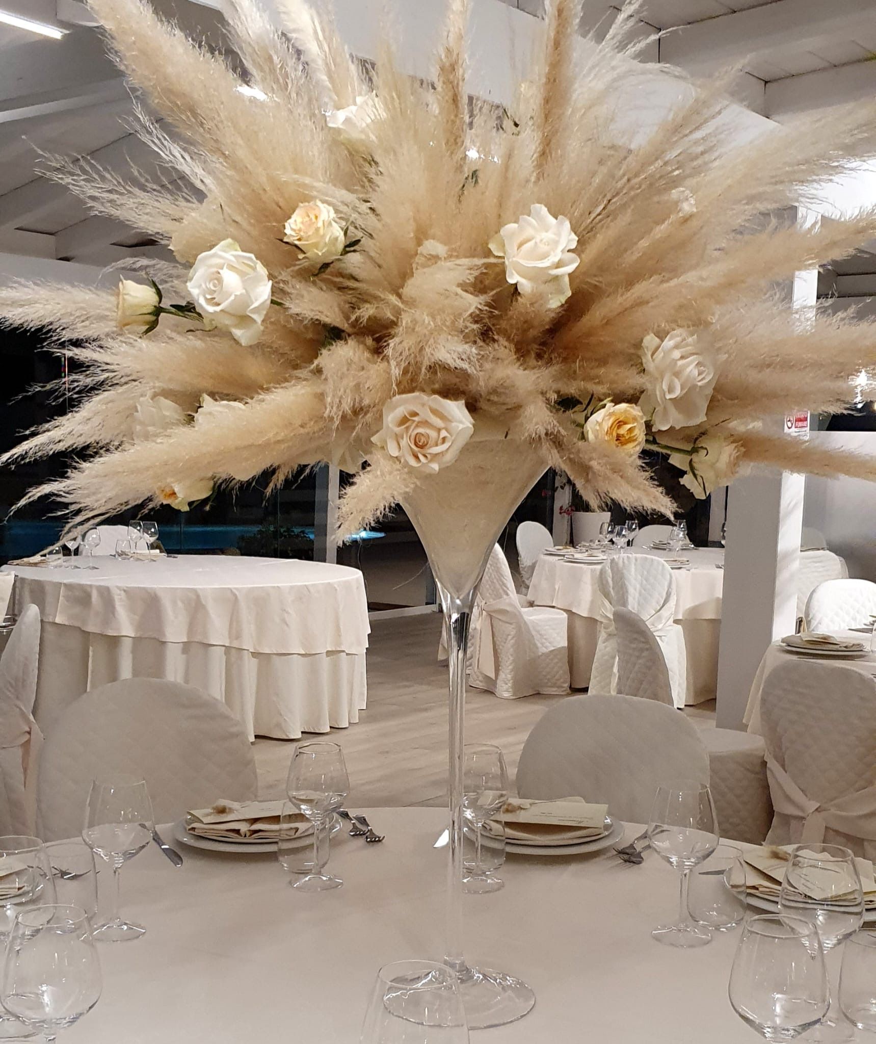 Centrotavola con erba della pampa e rose su un tavolo apparecchiato per un evento formale.