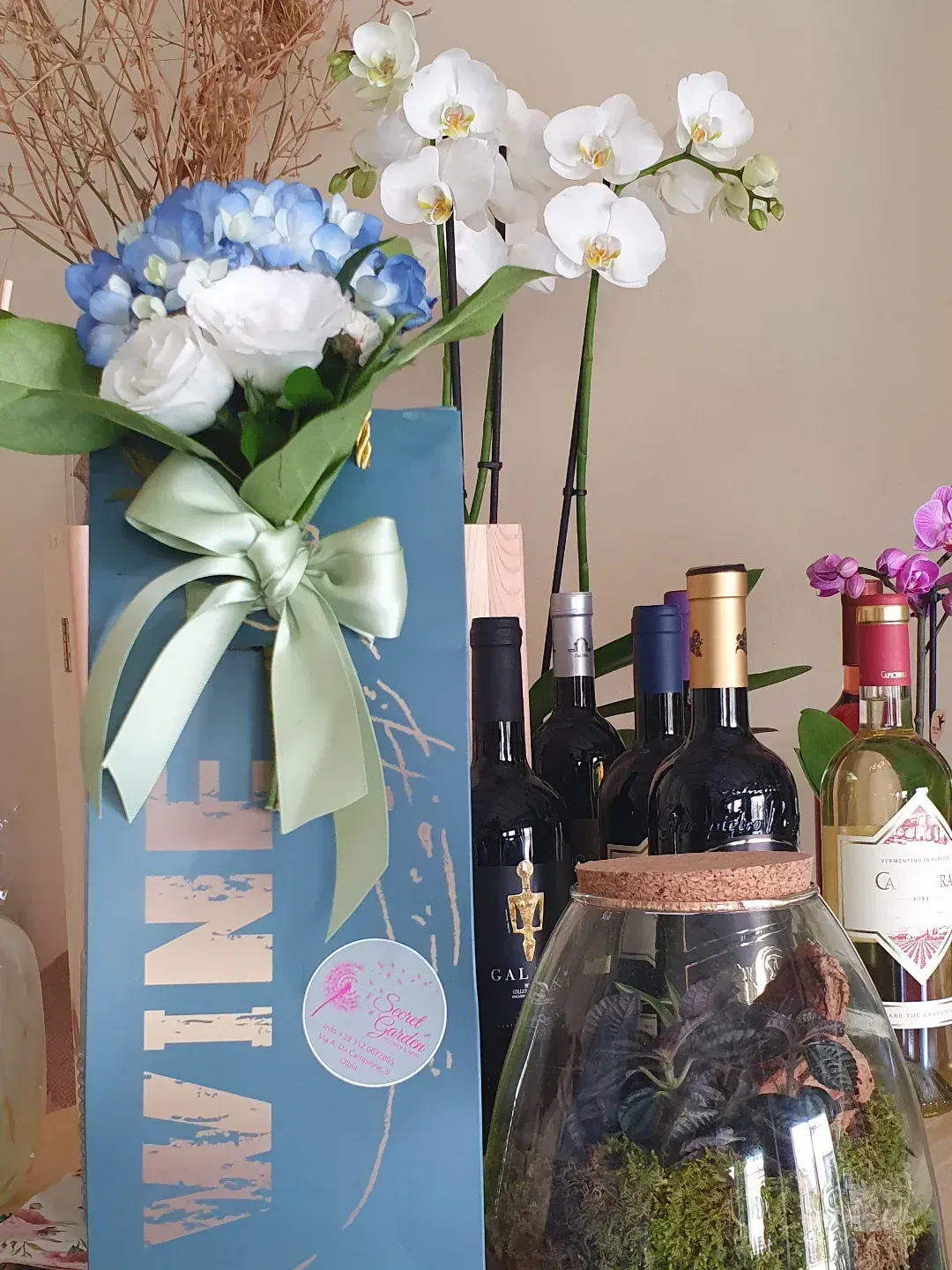Un bouquet in una borsa da vino con bottiglie, orchidee e un terrario.