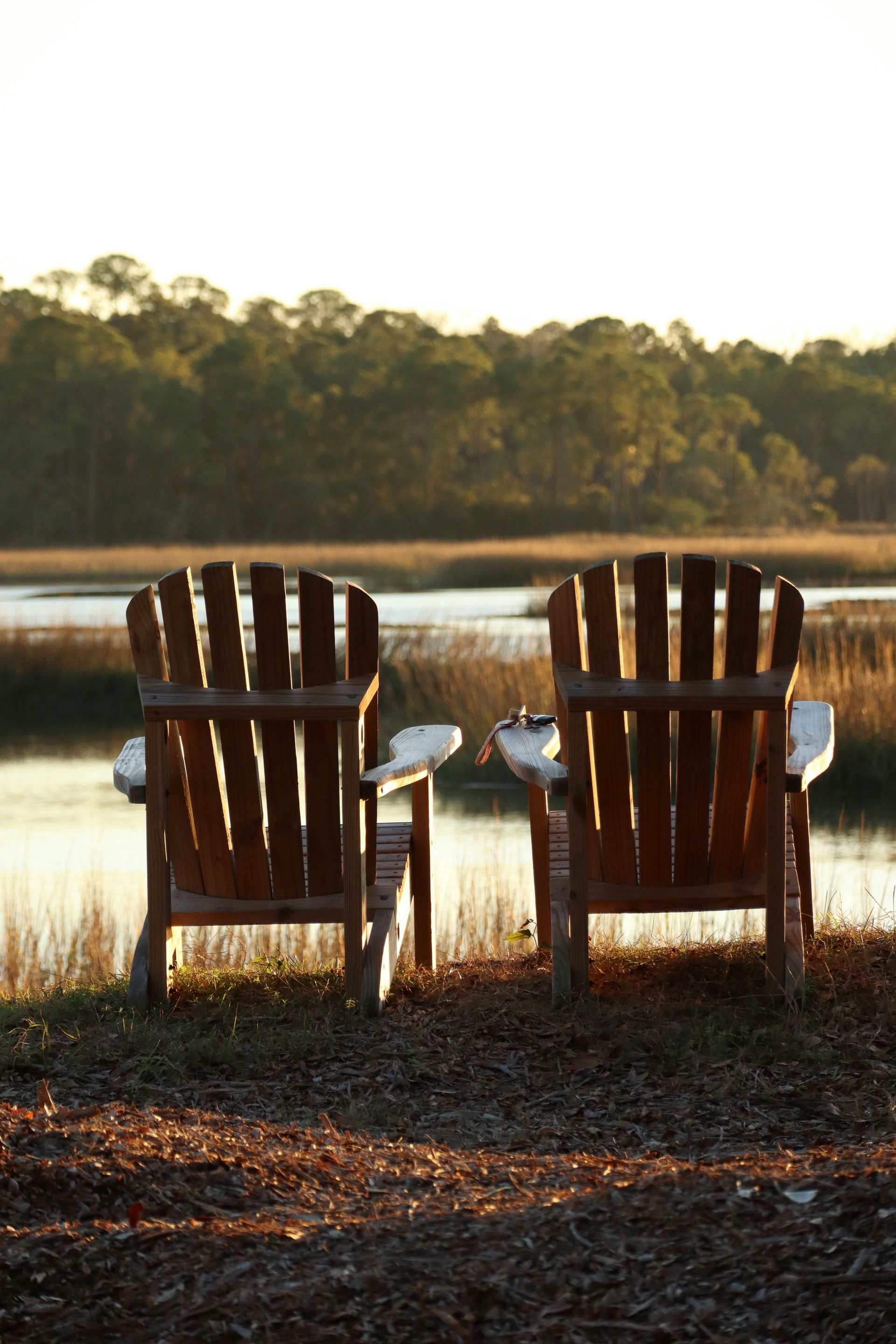 Two wooden chairs are sitting next to a body of water.