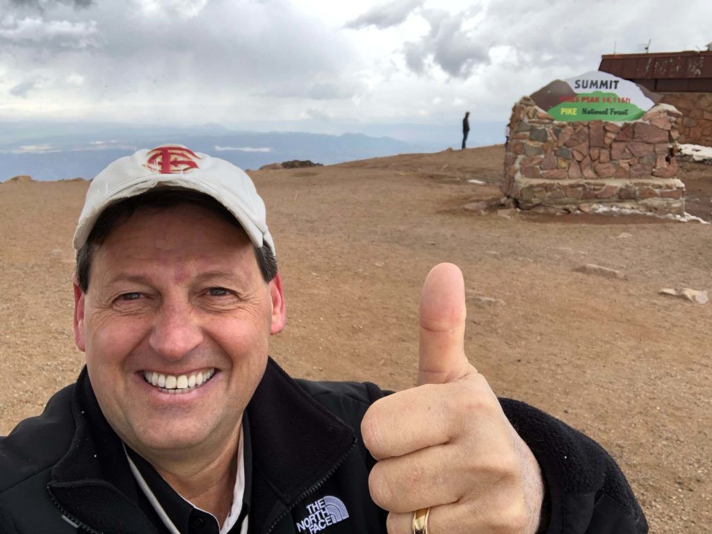 A man giving a thumbs up in front of a sign that says summit