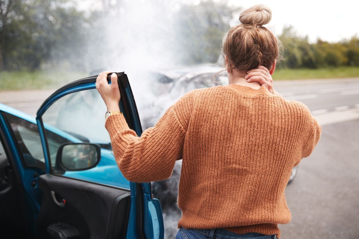 A woman is standing next to a car that has been involved in a car accident.