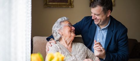 A man is dancing with an elderly woman in a living room.