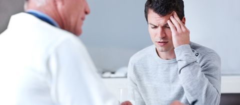 A man is holding his head while talking to a doctor.