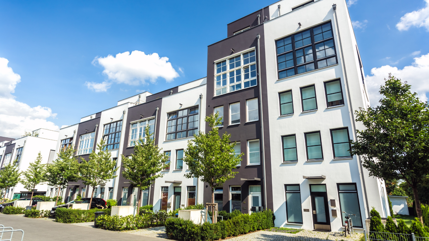 Modern townhouses with white and dark exterior paint, trees, and blue sky.