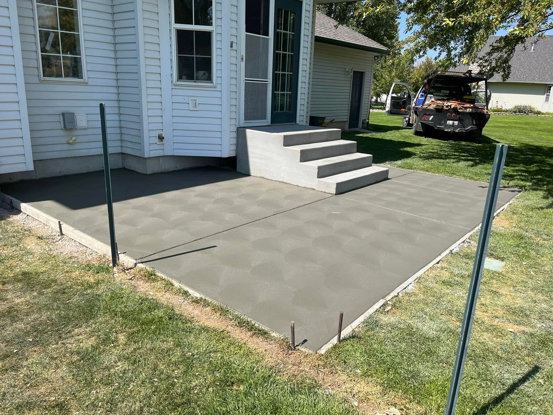 A newly poured concrete patio extending from a white house with grey concrete steps leading up to a door.