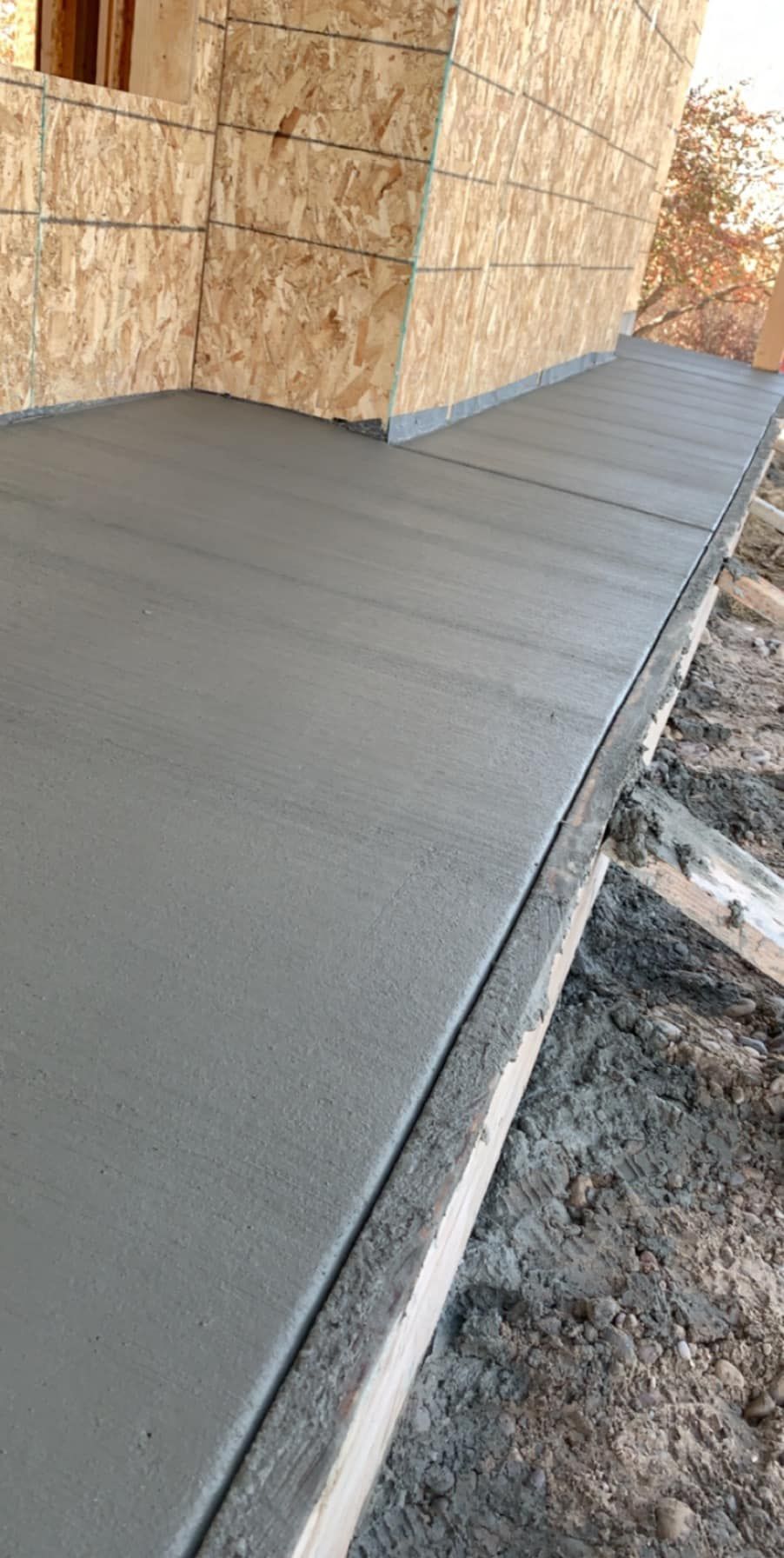 A smooth, gray concrete walkway bordering a wall constructed with oriented strand board (OSB) panels.