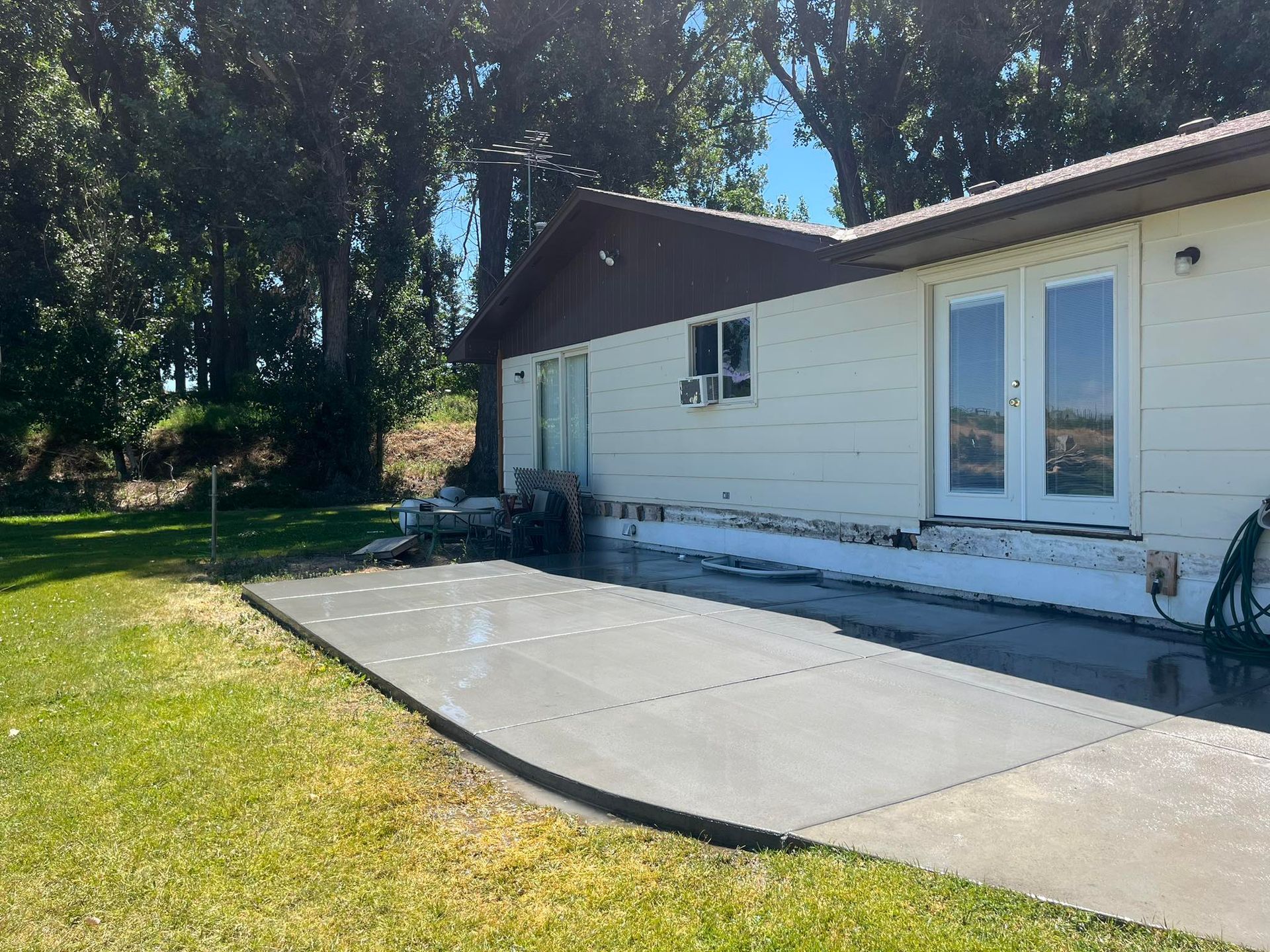 A newly poured, rectangular concrete patio sits beside the white exterior wall of a house with French doors.