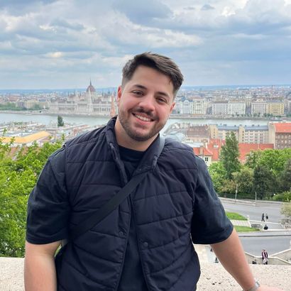 A man in a black vest is standing in front of a city.