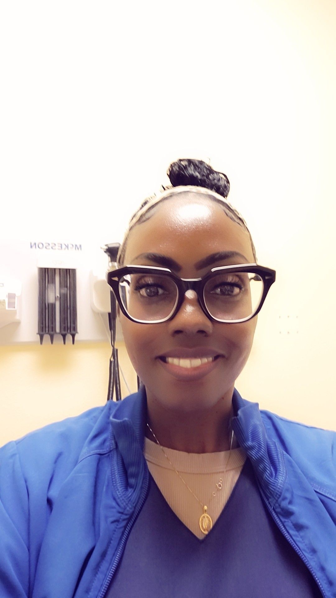A woman wearing glasses and a blue jacket is smiling.
