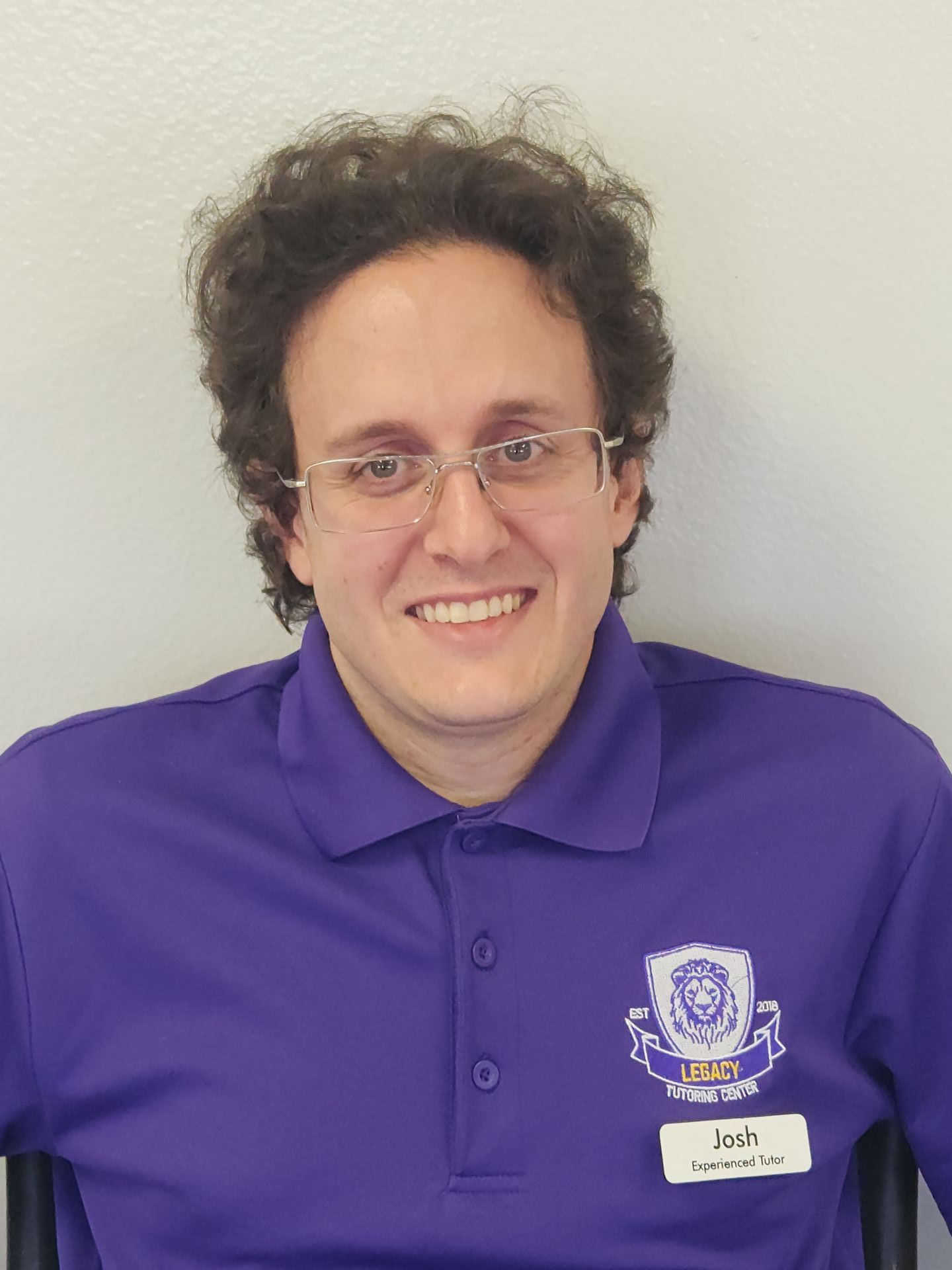 A man wearing glasses and a purple polo shirt is smiling