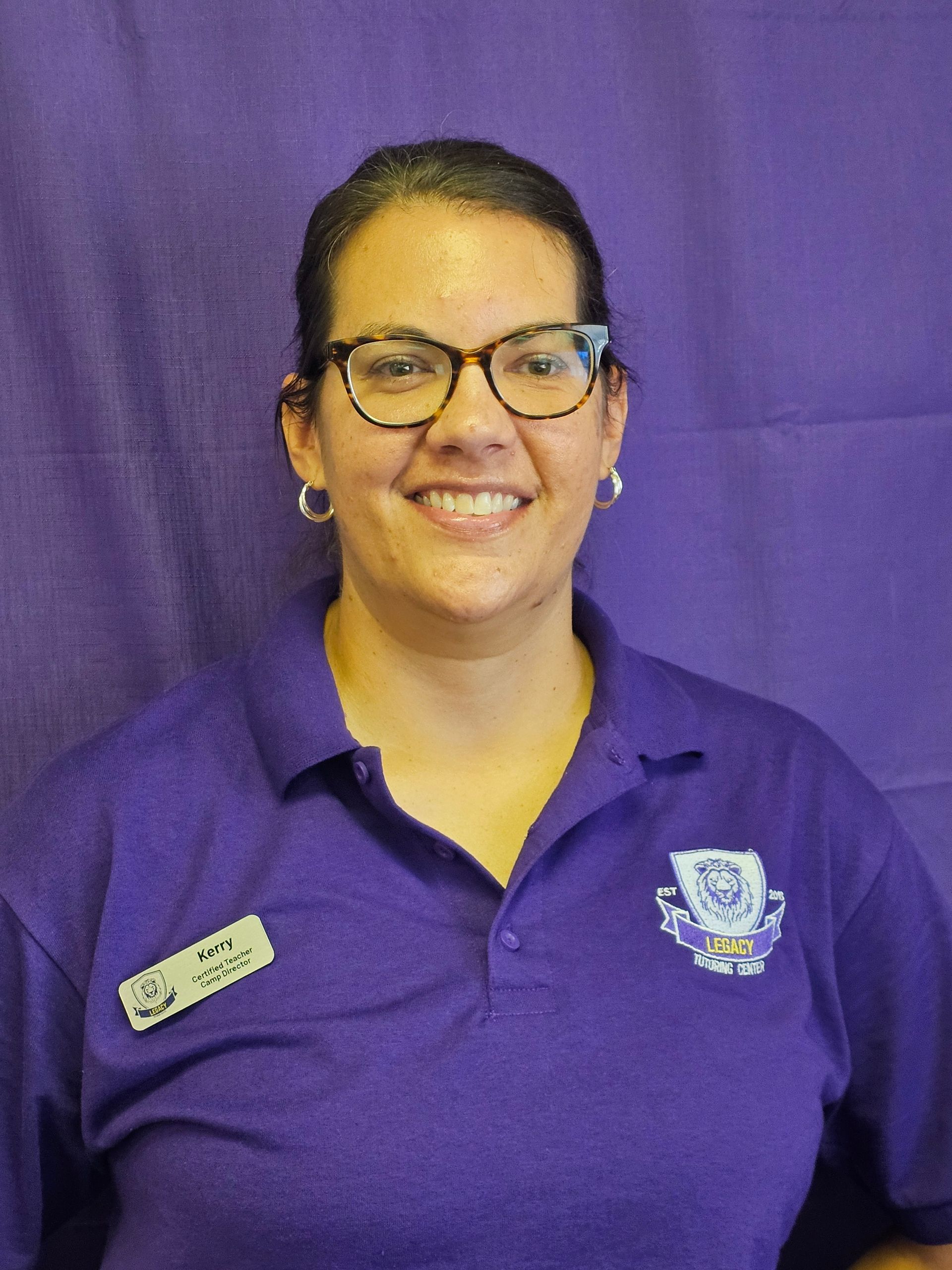A woman wearing glasses and a purple shirt is smiling.