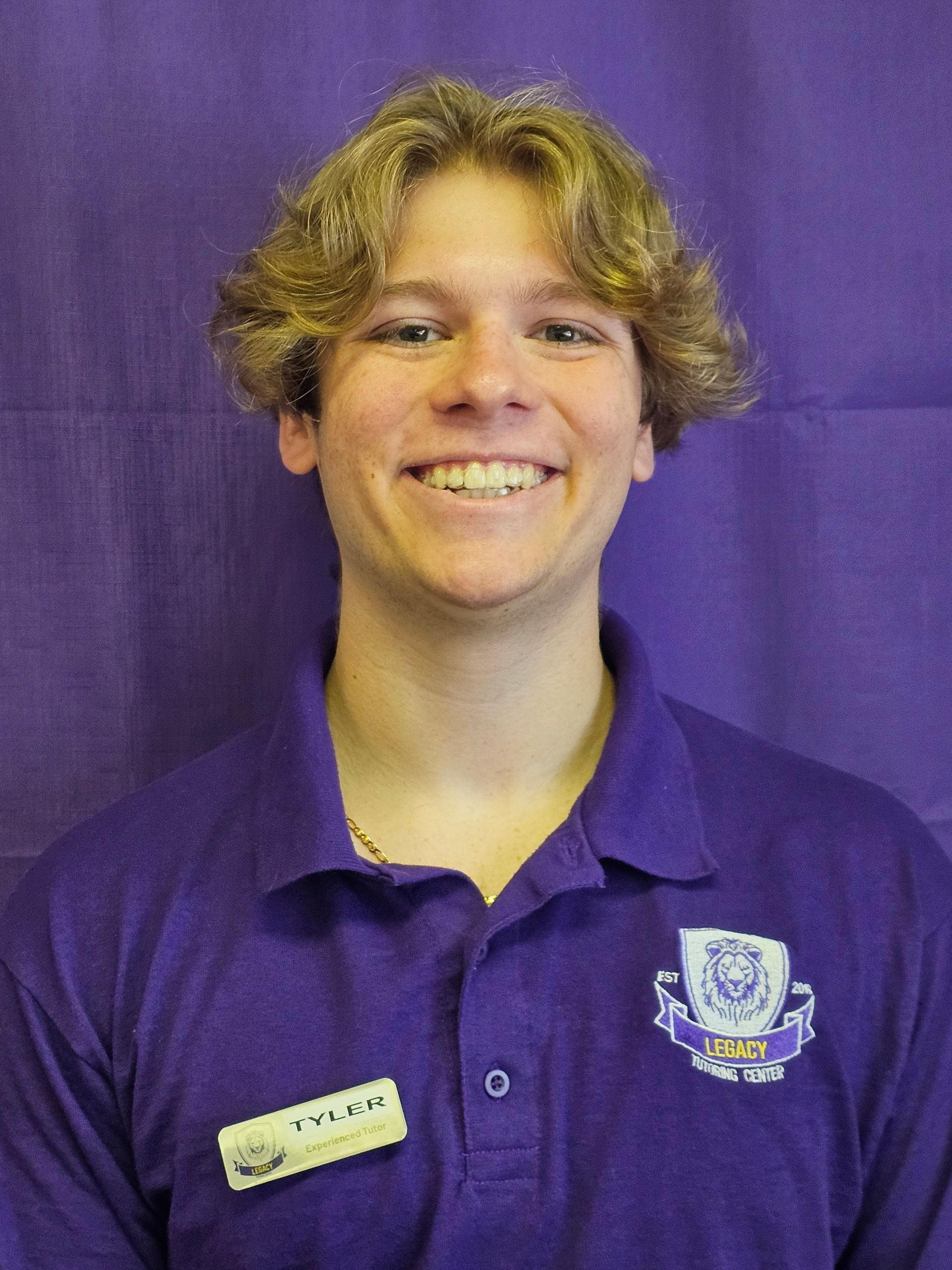 A young man wearing a purple polo shirt is smiling in front of a purple background