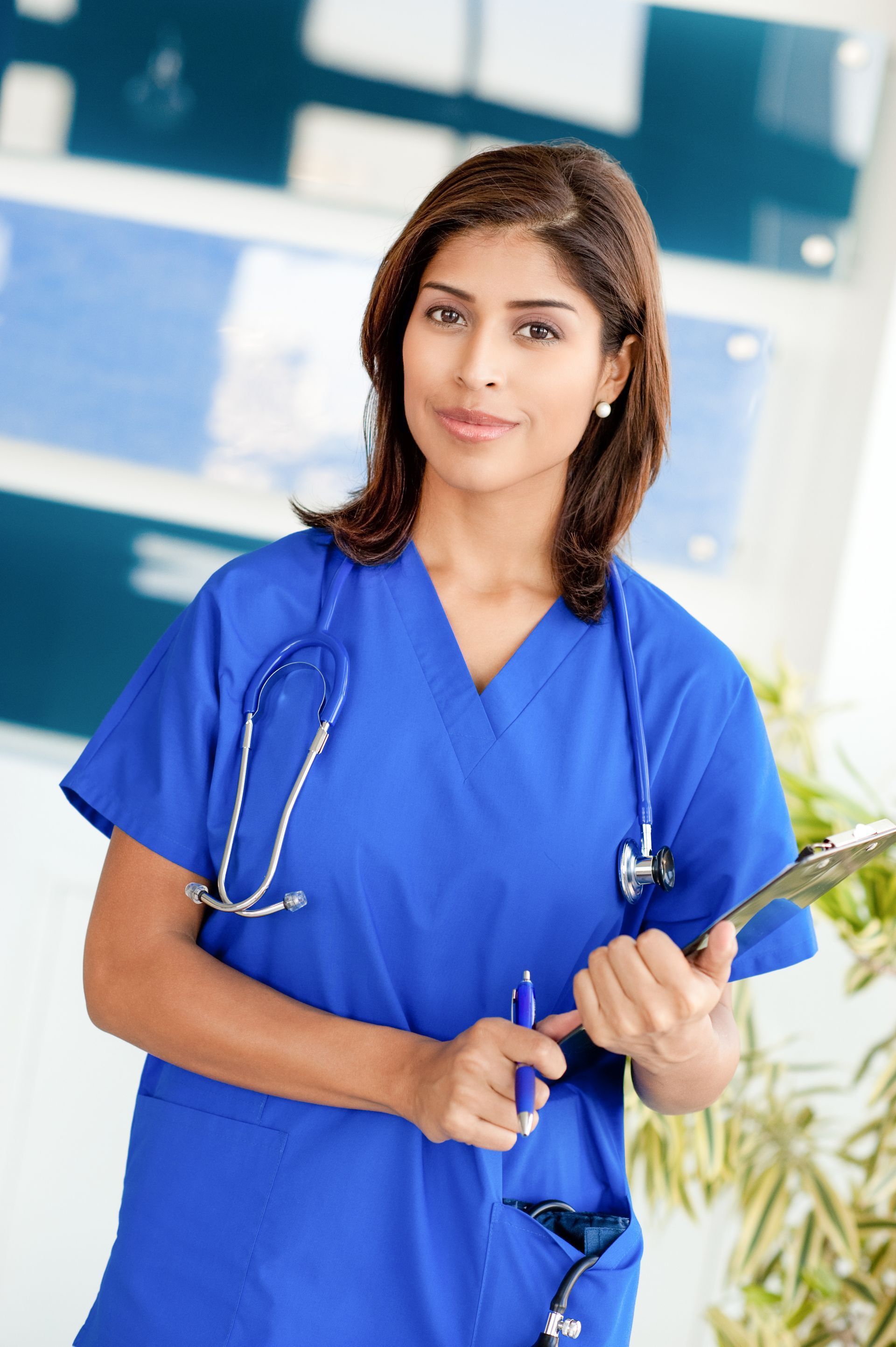 A nurse in a blue scrub is holding a clipboard and a pen.