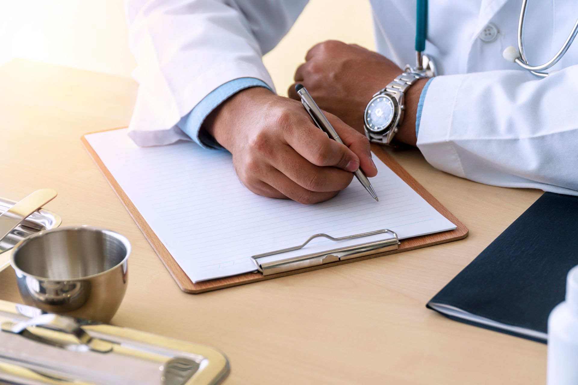 A doctor is writing on a clipboard with a pen.