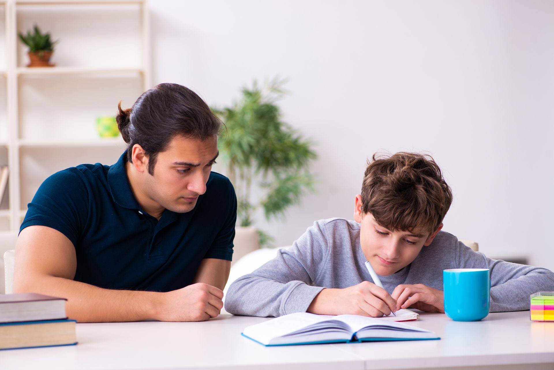 A man is helping a young boy with his homework at home.