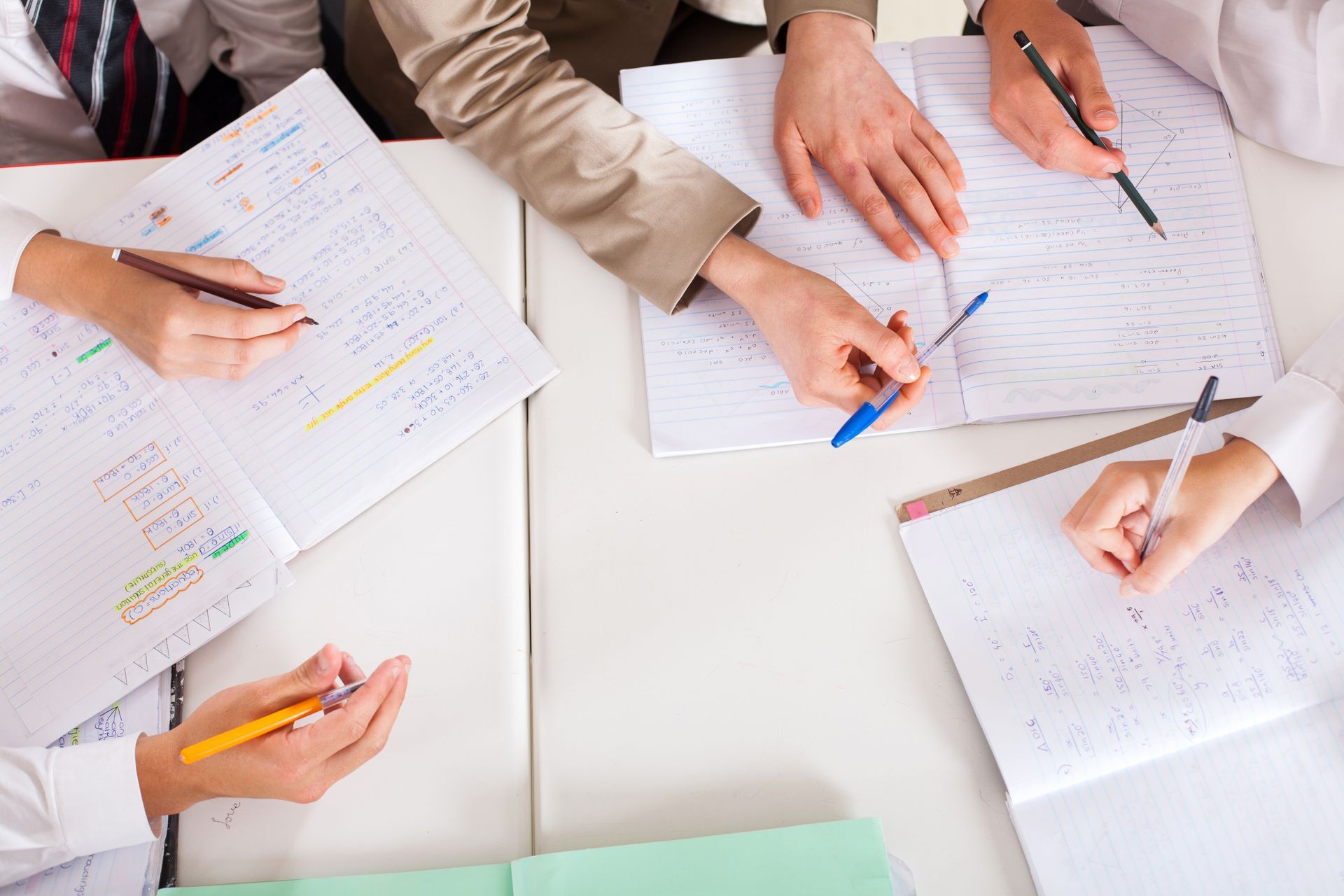 A group of people are sitting around a table writing in notebooks.