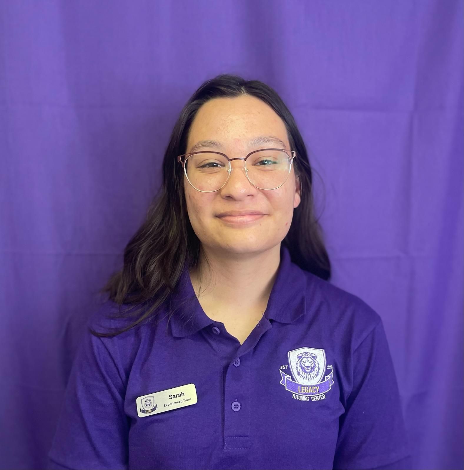 A woman wearing glasses and a purple shirt is standing in front of a purple curtain.