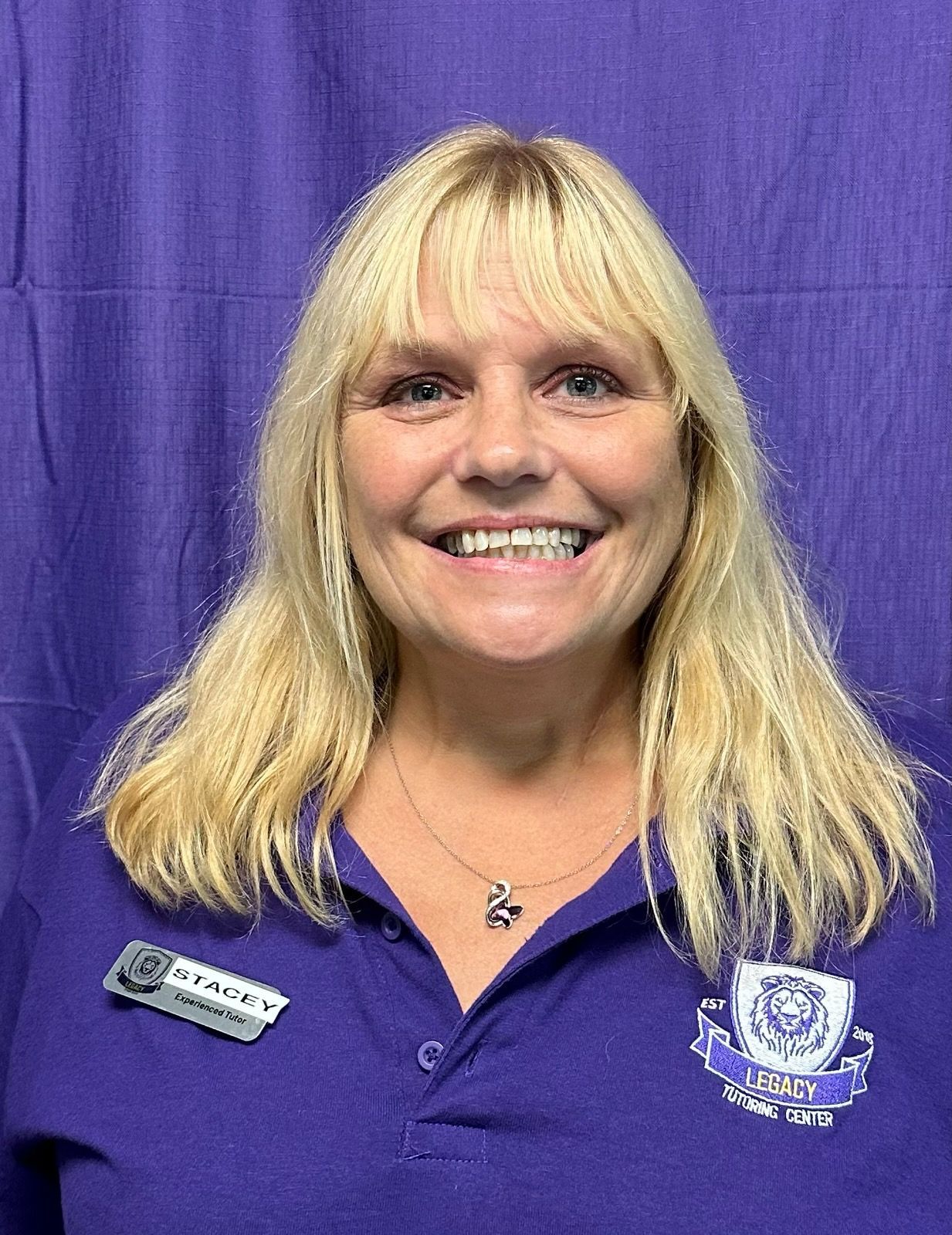 A woman in a purple shirt is smiling in front of a purple curtain.