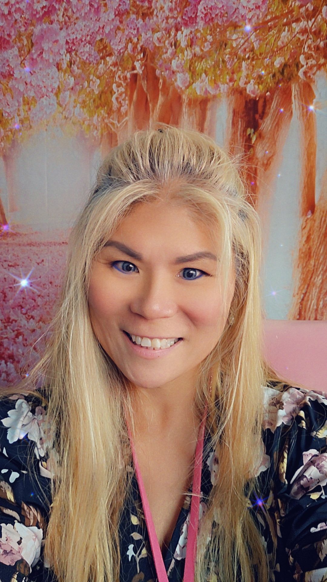 A woman with blonde hair is smiling in front of a pink background.