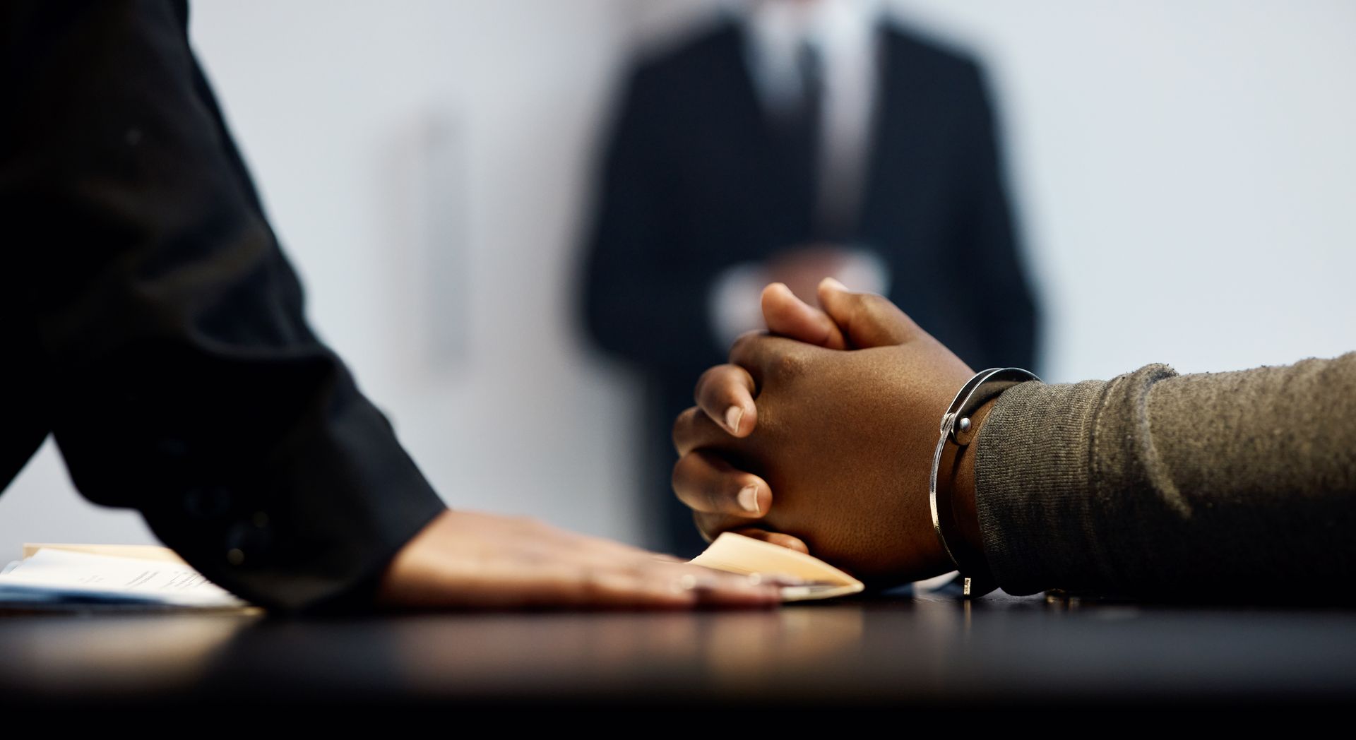 Two people clasping hands across a table in a business meeting, with a blurred person in the background