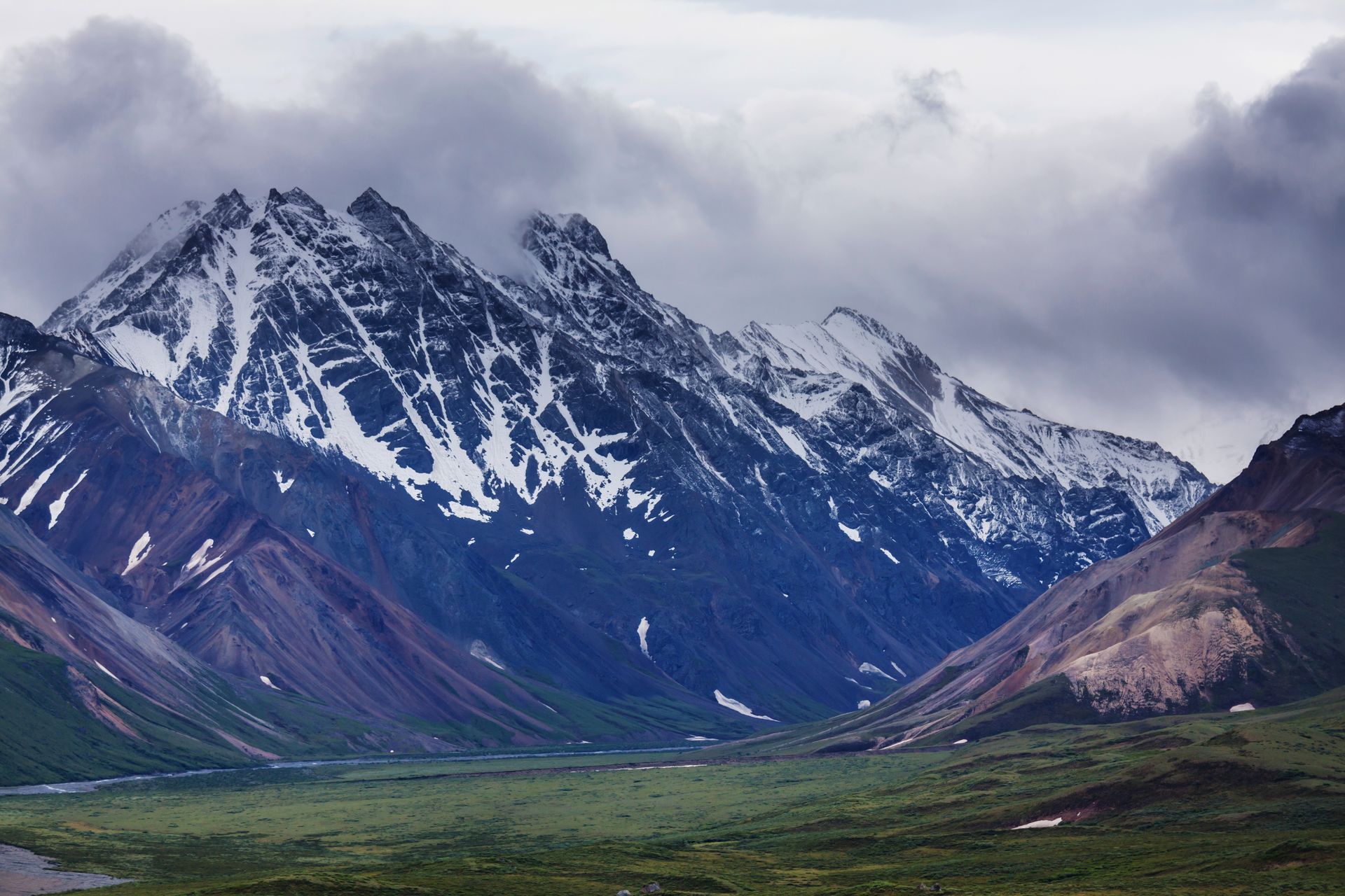 Snowy mountain range above a green valley under cloudy skies