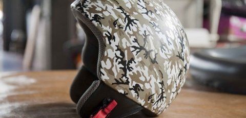 Un casco con motivo mimetico è appoggiato su un tavolo di legno.