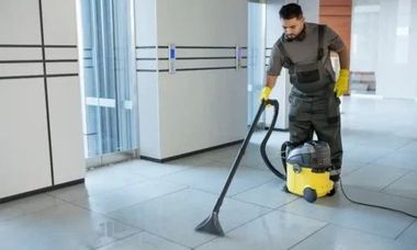 Man in work clothes vacuums a wet tiled floor in an office setting.