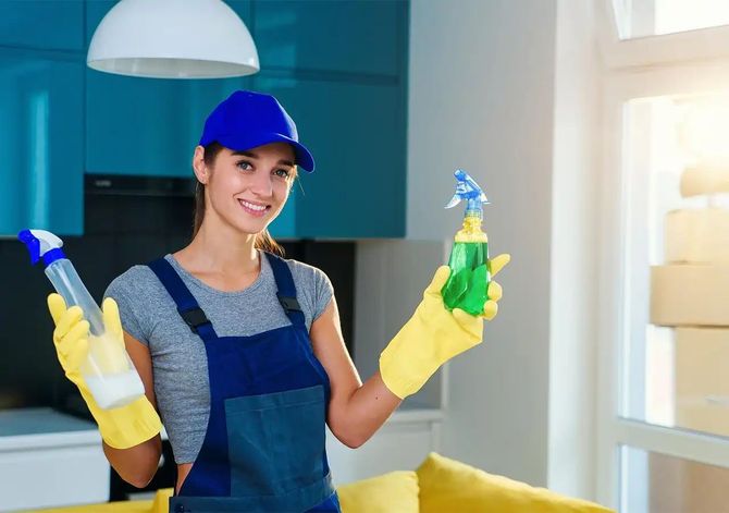 Woman in cleaning uniform holding spray bottles, smiling.