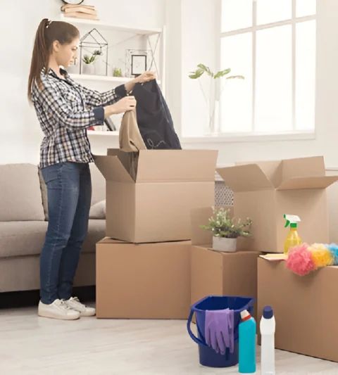 Woman packing clothes into cardboard boxes in a well-lit room, preparing for a move.
