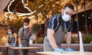 Restaurant staff wearing masks and gloves cleaning tables.