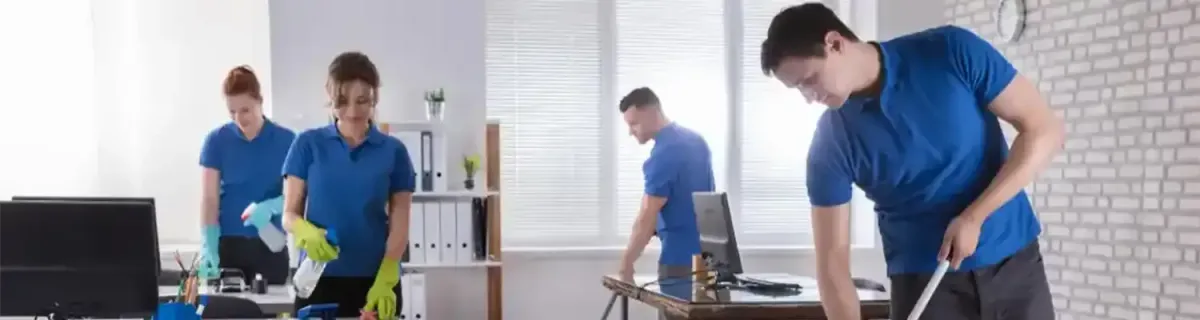 Office cleaning crew in blue shirts and gloves, cleaning desks and floors.