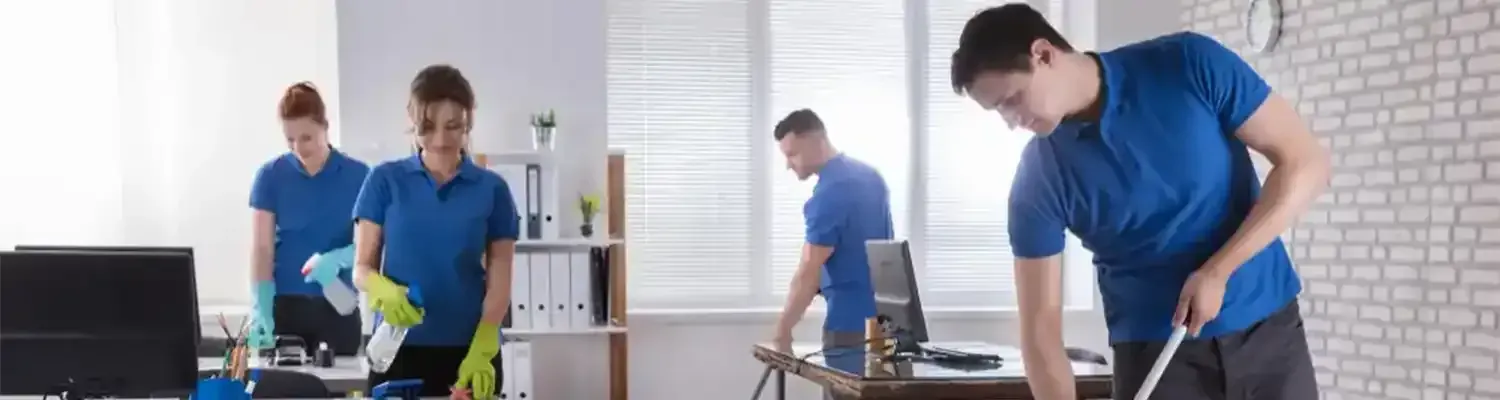 Office cleaning crew in blue shirts and gloves, cleaning desks and floors.