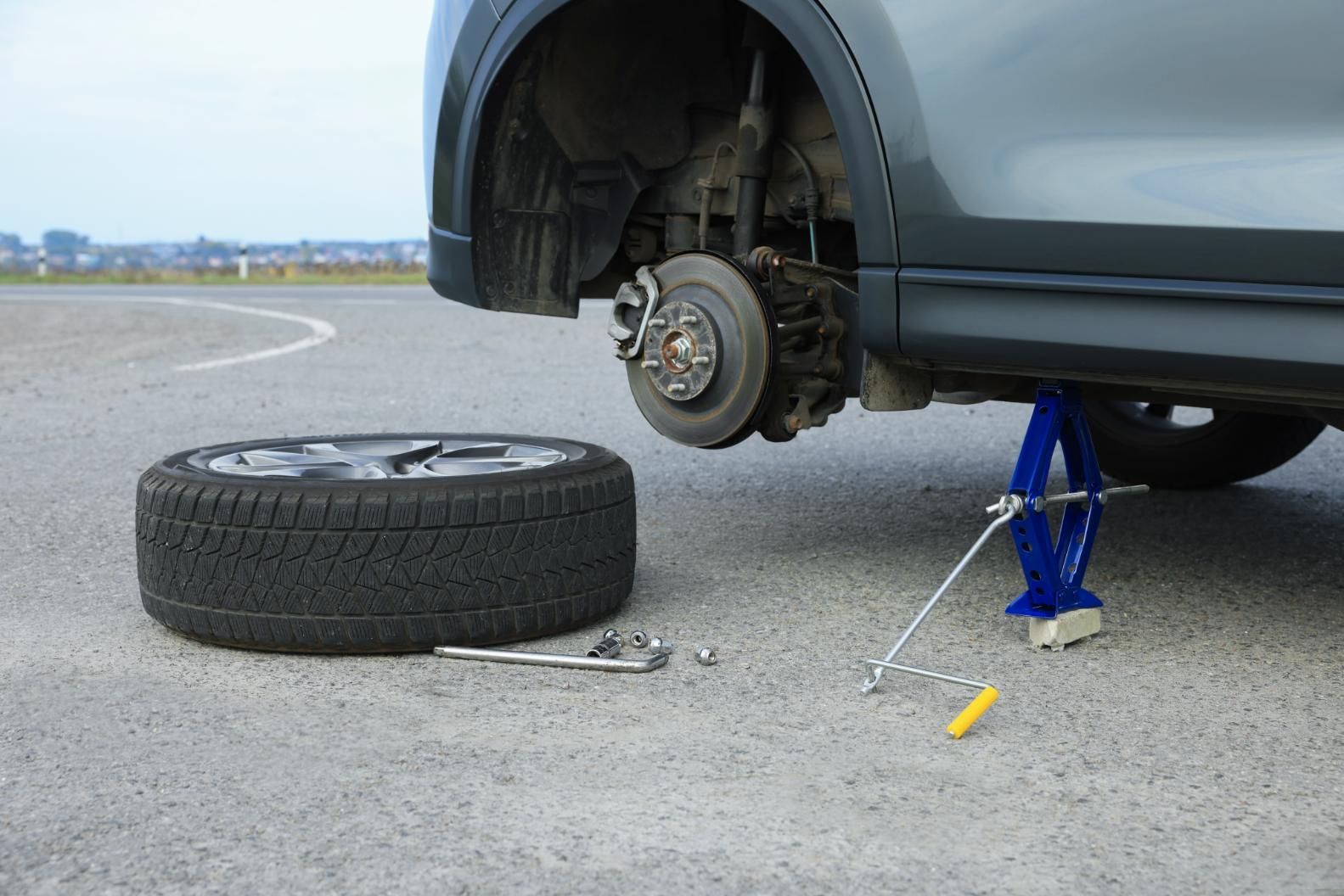 Car with flat tire being changed with jack and tools on pavement.