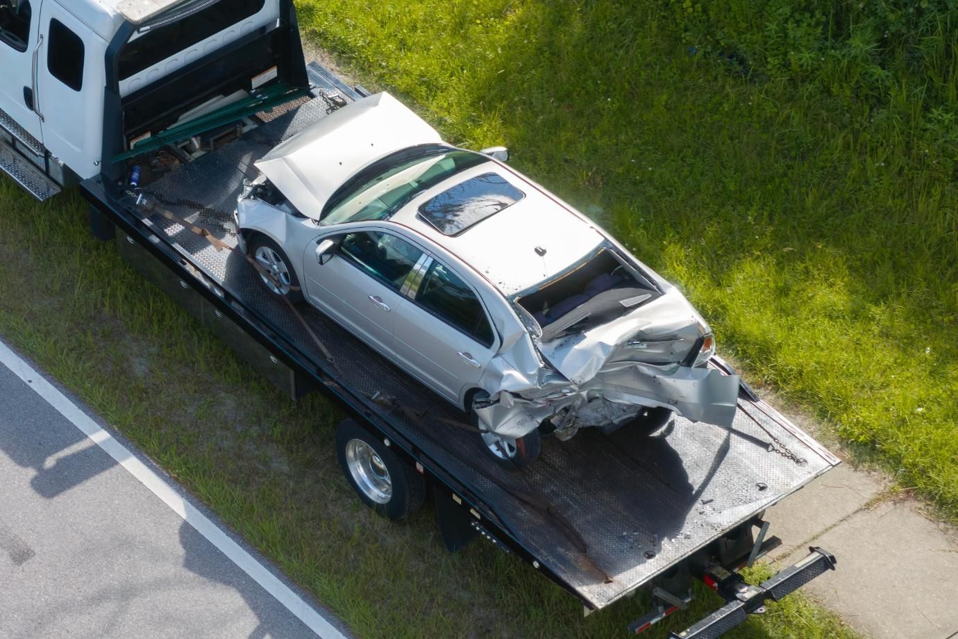 Silver car, heavily damaged, on a tow truck, roadside setting.